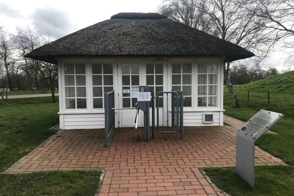 A small, white building with a thatched roof, a brick pathway leading to it, and a signboard to the right.