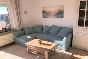 Una sala de estar con un sofá modular, una mesa de centro, un cuadro en la pared y un ventanal con cortinas.