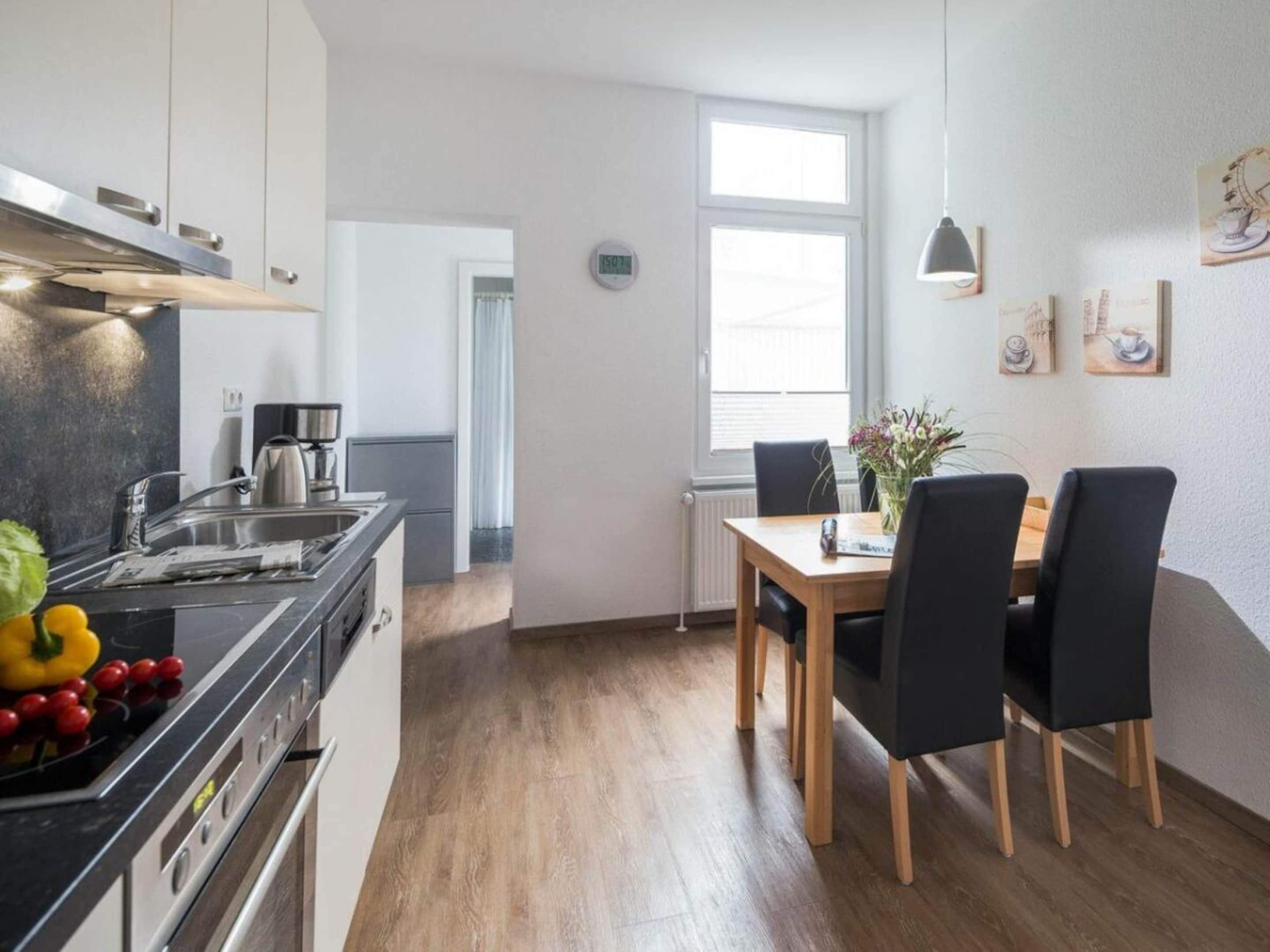 Une cuisine moderne équipée d’une cuisinière, d’un évier et d’une machine à café, qui donne sur un coin repas avec une table et des chaises.