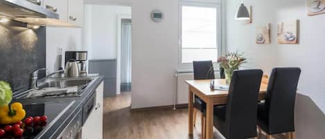 Une cuisine moderne équipée d’une cuisinière, d’un évier et d’une machine à café, qui donne sur un coin repas avec une table et des chaises.