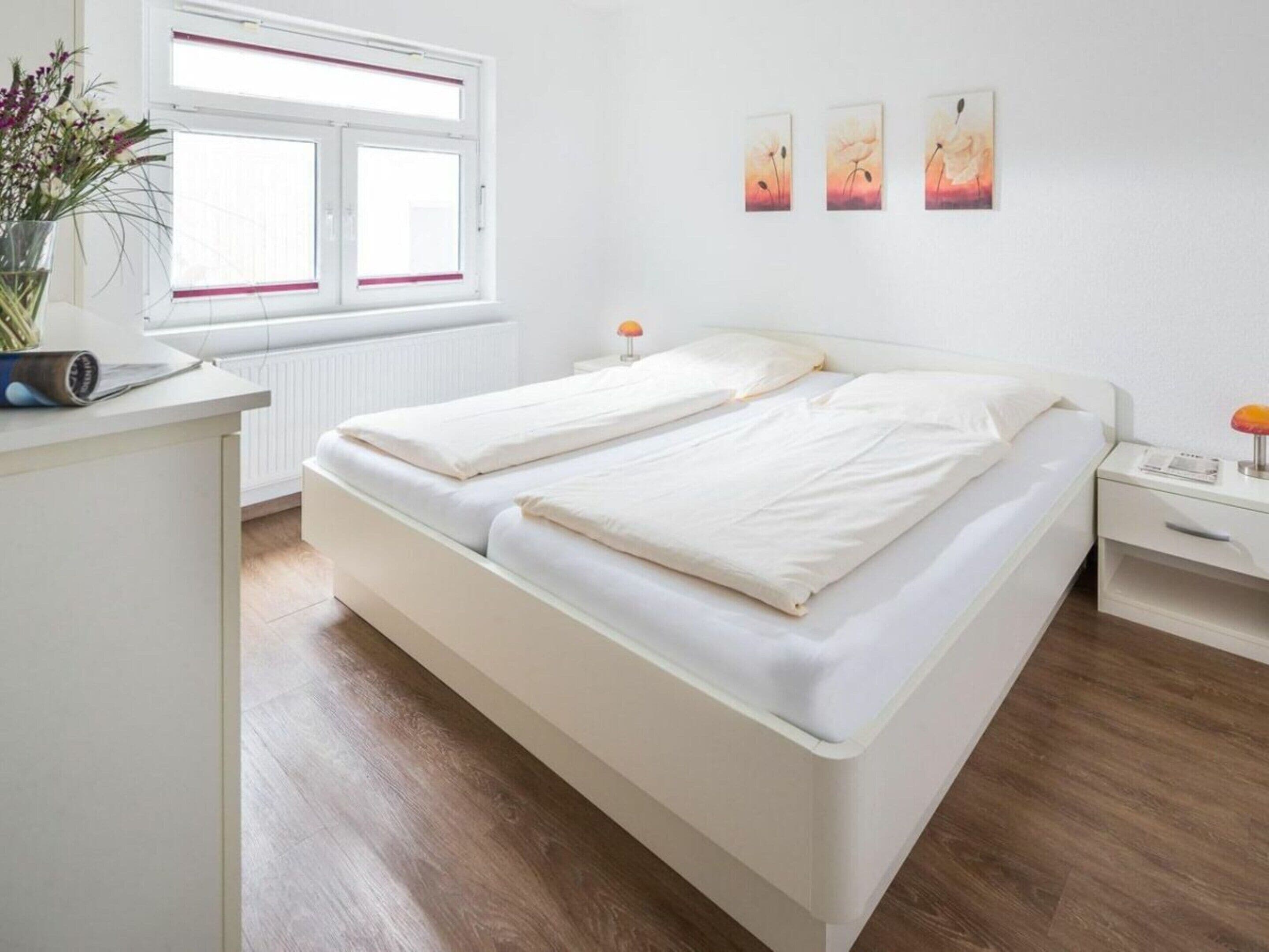 Un dormitorio moderno con una cama doble, una mesita de noche, una ventana con persianas y tres cuadros colgados en la pared.