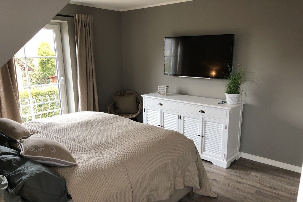 A bedroom with a bed, a television mounted on the wall, a white cabinet, and a window with curtains.