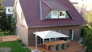 A two-story house with a red-tiled roof, a patio with a table and chairs, and a small garden. - Holiday home with 3 bedrooms (Scharbeutz)