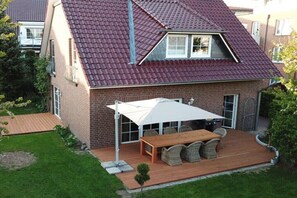 A two-story house with a red-tiled roof, a patio with a table and chairs, and a small garden. - Holiday home with 3 bedrooms (Scharbeutz)