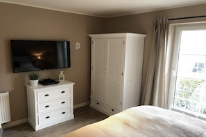 Ein Schlafzimmer mit einem Bett, einem an der Wand befestigten Fernseher, einem weißen Kommode und einem Kleiderschrank.