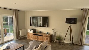 A living room with a sofa, a TV mounted on the wall, a wooden cabinet, and a floor lamp. - Holiday home with 3 bedrooms (Scharbeutz)