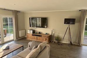 A living room with a sofa, a TV mounted on the wall, a wooden cabinet, and a floor lamp. - Holiday home with 3 bedrooms (Scharbeutz)