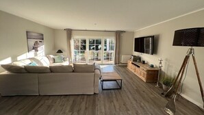 A modern living room with a sectional sofa, a coffee table, a television, and a lamp. - Holiday home with 3 bedrooms (Scharbeutz)