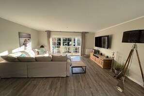 A modern living room with a sectional sofa, a coffee table, a television, and a lamp. - Holiday home with 3 bedrooms (Scharbeutz)