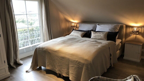 A bedroom with a large bed, two bedside lamps, a window with curtains, and a view of greenery outside. - Holiday home with 3 bedrooms (Scharbeutz)