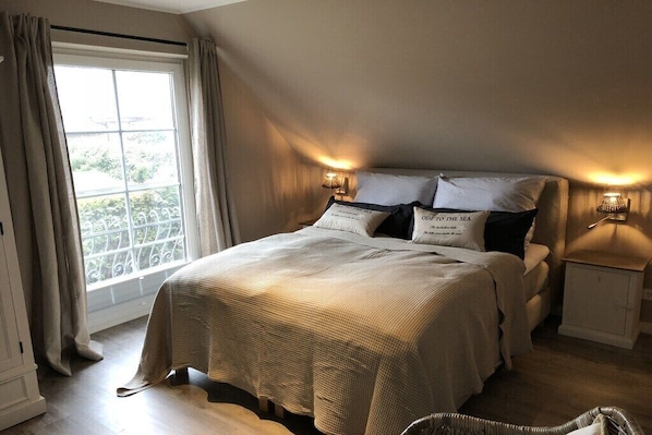 A bedroom with a large bed, two bedside lamps, a window with curtains, and a view of greenery outside. - Holiday home with 3 bedrooms (Scharbeutz)
