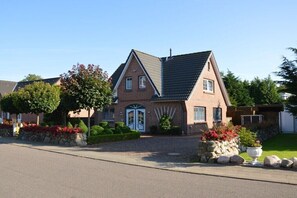 Une maison à deux étages avec une façade en briques, un toit à deux versants et une entrée principale dotée d’une double porte.