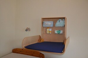 Une petite chambre avec un lit simple, une tête de lit en bois et une étagère au-dessus du lit où sont rangés les articles de toilette.