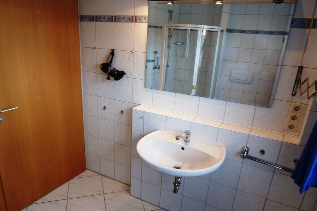 A bathroom with a white sink, a mirror above it, and a shower visible through the glass door.