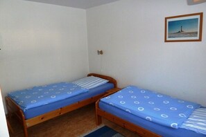 Habitació amb dos llits de fusta amb roba de llit blava, una catifa petita i un quadre al mur.