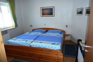 A bedroom with a wooden bed, a window with curtains, a wall-mounted picture, and a door. - Holiday home Sommerwind II (St. Peter-Ording)