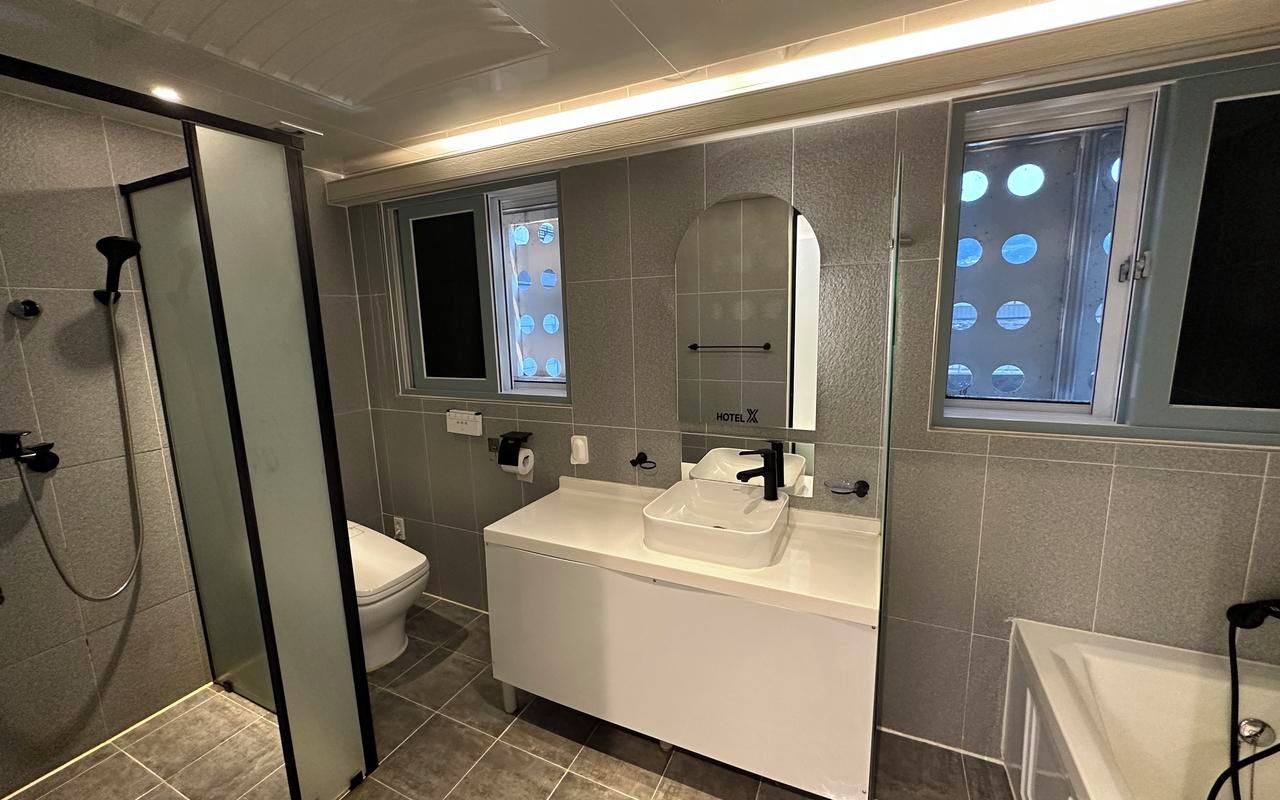 Un baño moderno con ducha envuelta en vidrio, lavamanos blanco con espejo arriba y un inodoro.