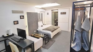 Una habitación de hotel moderna con una cama, un escritorio con computadora, una silla, una mesita y un perchero.