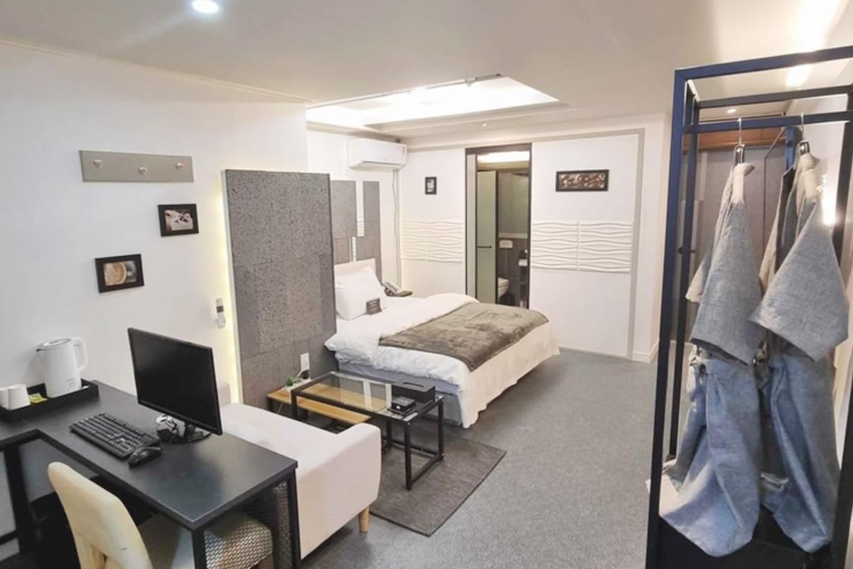 Una habitación de hotel moderna con una cama, un escritorio con computadora, una silla, una mesita y un perchero.
