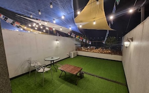 An outdoor patio with artificial grass, a wooden table, metal chairs, and string lights.
