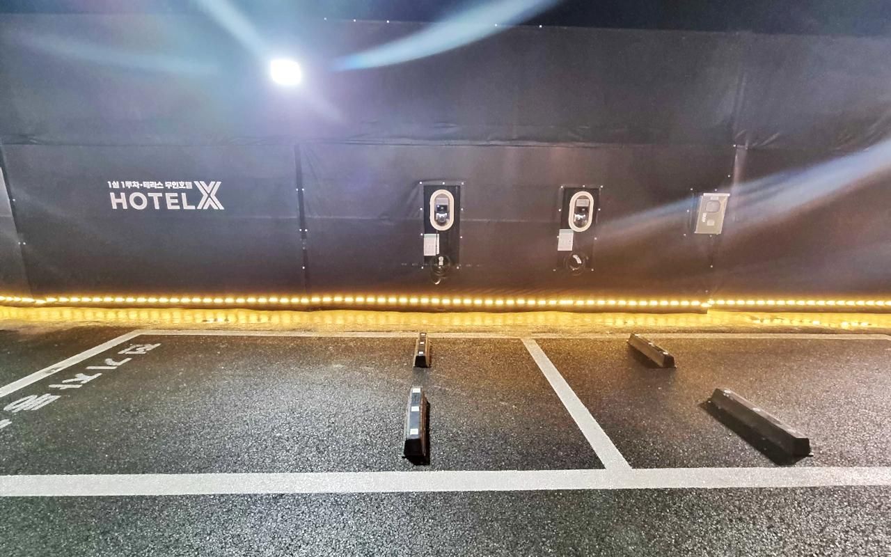 L’entrée d’un hôtel, avec une enseigne indiquant « HÔTELX », et un espace de stationnement avec des places délimitées.