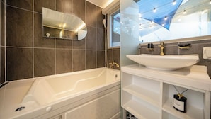 Un baño moderno con bañera, un espejo grande y un lavamanos.
