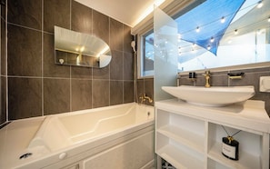 Un baño moderno con bañera, un espejo grande y un lavamanos.