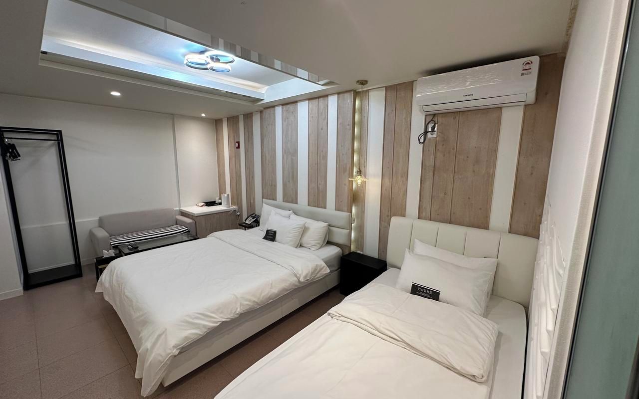 Habitación de hotel con dos camas, un escritorio, una silla, una mesita de noche y una lámpara en el techo.
