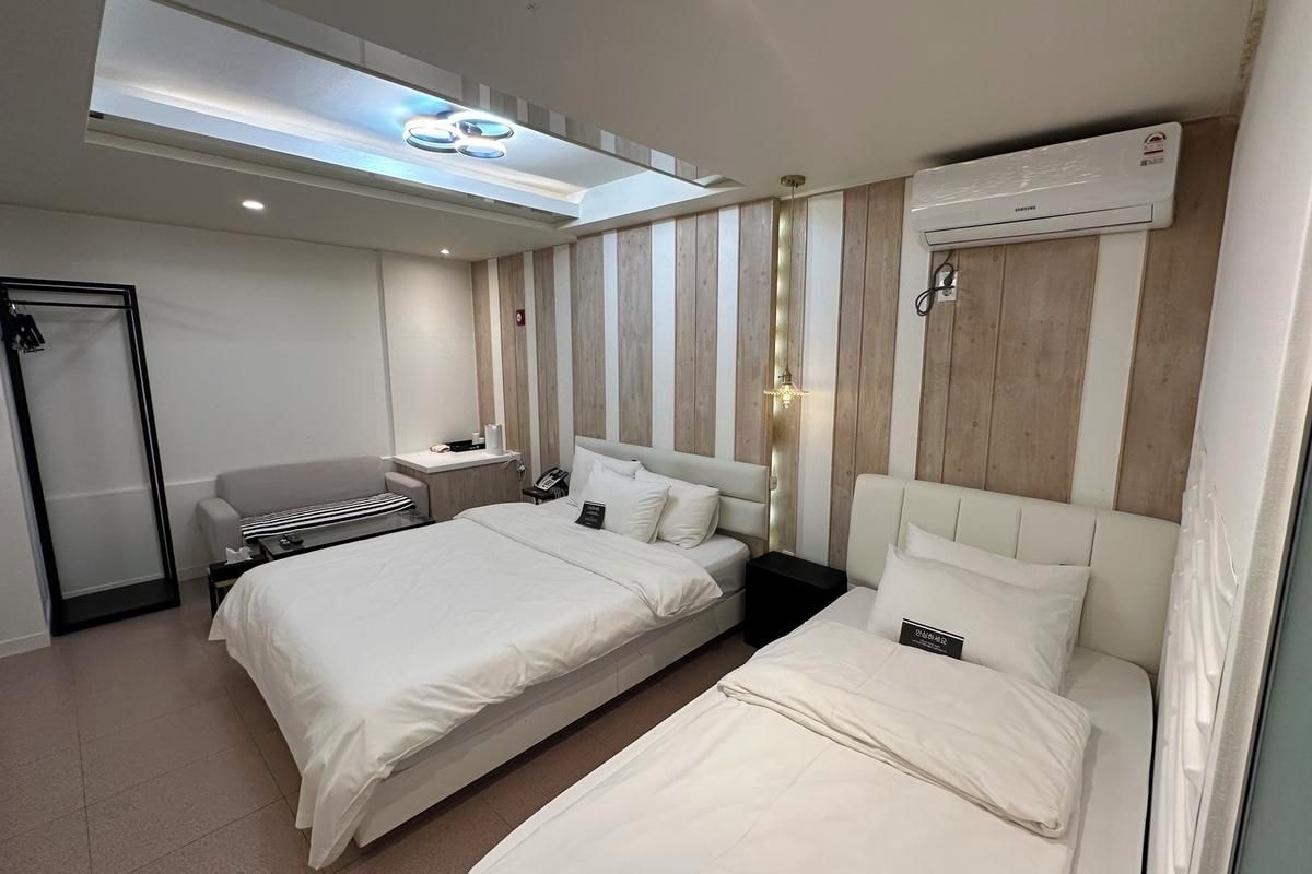 Habitación de hotel con dos camas, un escritorio, una silla, una mesita de noche y una lámpara en el techo.