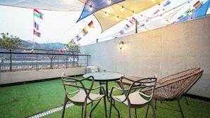 Un espacio al aire libre con una mesa redonda y sillas, un sillón de mimbre y vistas a una masa de agua con banderas.