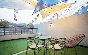 Un espacio al aire libre con una mesa redonda y sillas, un sillón de mimbre y vistas a una masa de agua con banderas.