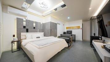 A modern hotel room with a large bed, a desk, a chair, a TV, and a bathroom with a mirror.