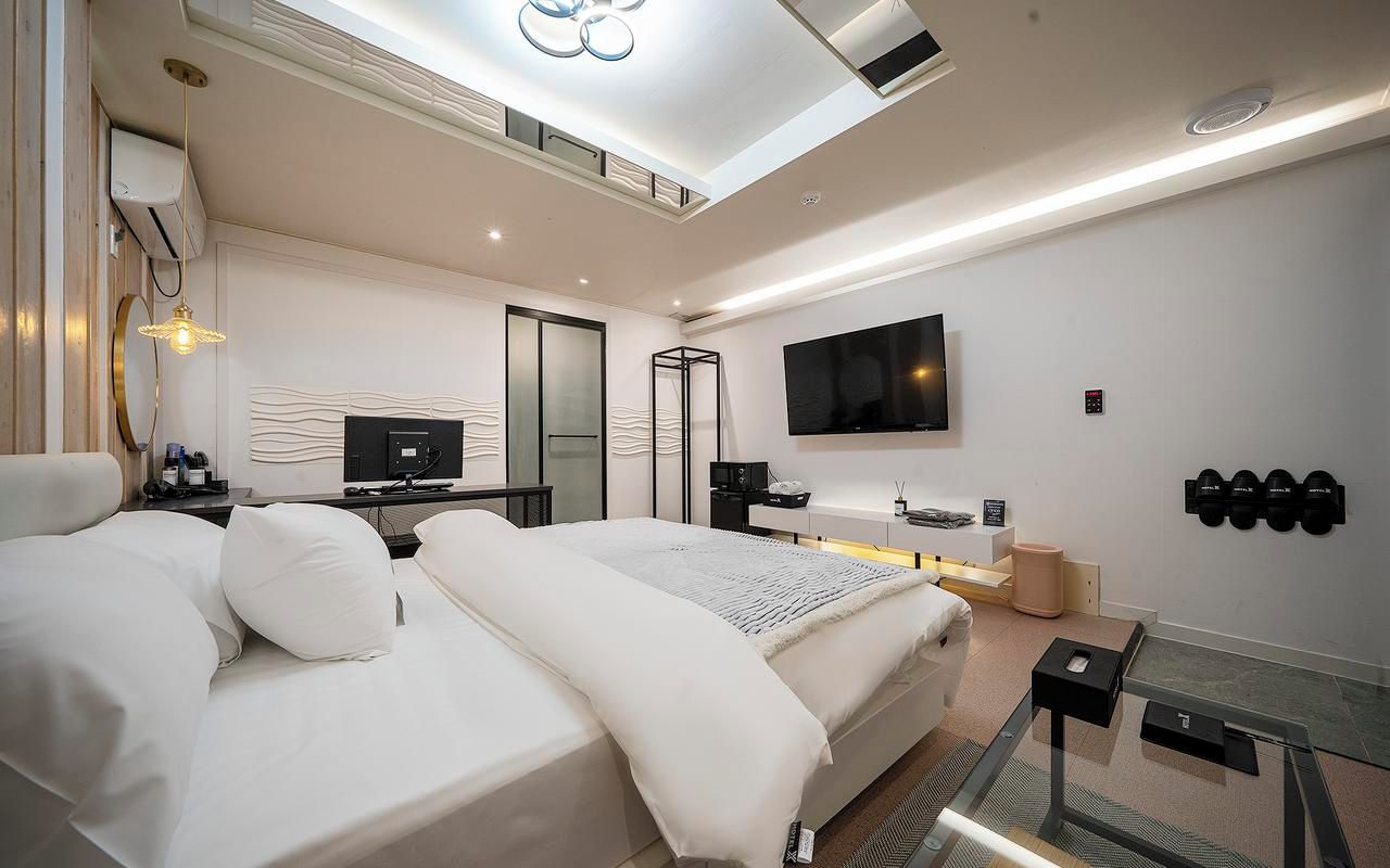 Ein modernes Schlafzimmer mit Bett, Nachttisch, Fernseher und einem an der Wand befestigten Schuhregal.