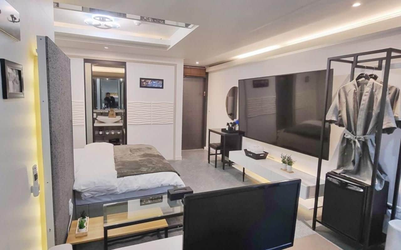 A modern hotel room with a bed, desk, TV, and a robe rack.