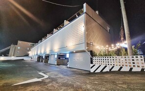 Un hotel con diseño moderno, que cuenta con un amplio estacionamiento y entrada protegida por un portón.