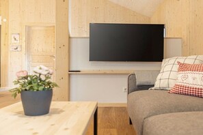 A room with a flat-screen TV mounted on the wall, a sofa with patterned cushions, a wooden table with a potted plant, and a door with a picture frame. - Cabin in Turrach with balcony and Wi-Fi (Turrach)