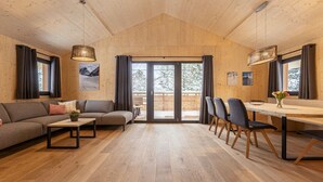 Una habitación amplia con techo de madera, un sofá, una mesa de comedor con sillas y un amplio ventanal corredero que da a un espacio exterior.