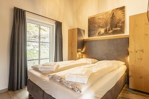 A bedroom with a bed, a window with curtains, a wall-mounted lamp, and a painting. - Superior Holiday Home # 5A with Sauna (Uttendorf)