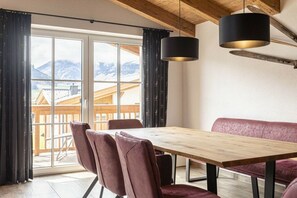 A dining area with a wooden table and chairs, a bench, and a view of mountains through large windows. - Superior Holiday Home # 5A with Sauna (Uttendorf)