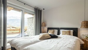 A bedroom with a large bed, a view of mountains through a window, and a stone wall. - Superior Holiday Home # 3B with Sauna (Uttendorf)