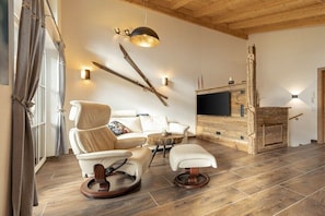 Ein modernes Wohnzimmer mit Sofa, Sessel, Hocker und Kamin.