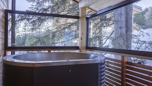 Un baño moderno con una bañera independiente, ventanas amplias y vistas a árboles cubiertos de nieve.