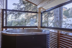 Een moderne badkamer met een vrijstaand bad, grote ramen en uitzicht op met sneeuw bedekte bomen.