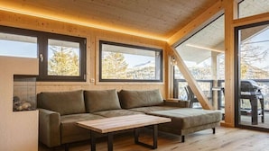 Interior de madera con un sofá y una mesa, ventanas amplias y vistas al exterior.