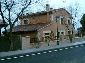Un edificio de dos pisos con techo de tejas, pared de ladrillo y valla de metal.