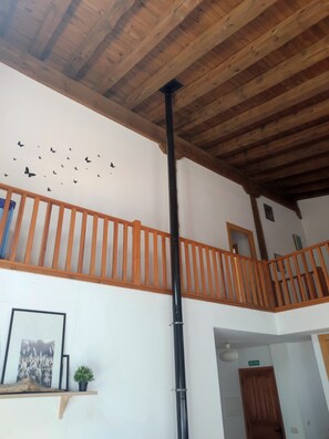 A wooden ceiling with a central black pipe, a white wall with a butterfly decal, and a wooden railing.