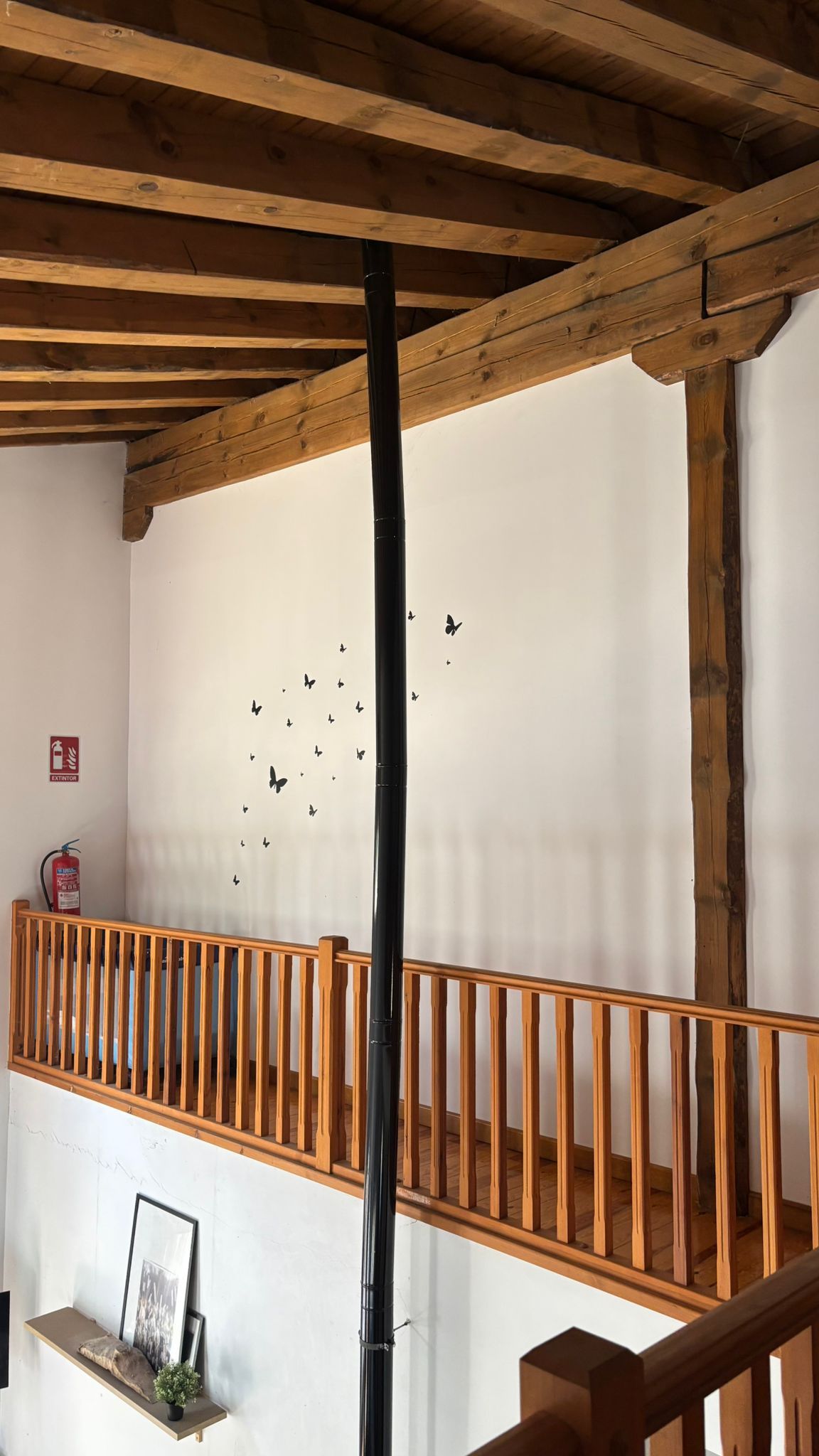 Un escalier en bois, avec un mur blanc et un tuyau noir qui descend verticalement.