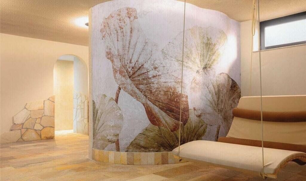 Une pièce dotée d’un mur incurvé orné d’un motif de feuilles, d’un pilier en pierre, d’un banc rembourré et d’une sculpture géométrique.