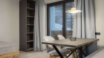 A modern dining area with a wooden table and chairs, a hanging light fixture, and a view of a snowy landscape through a window.
