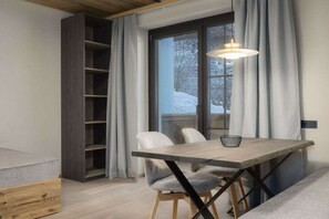Een moderne eetruimte met een houten tafel en stoelen, een hanglamp en zicht op een besneeerd landschap door een raam.